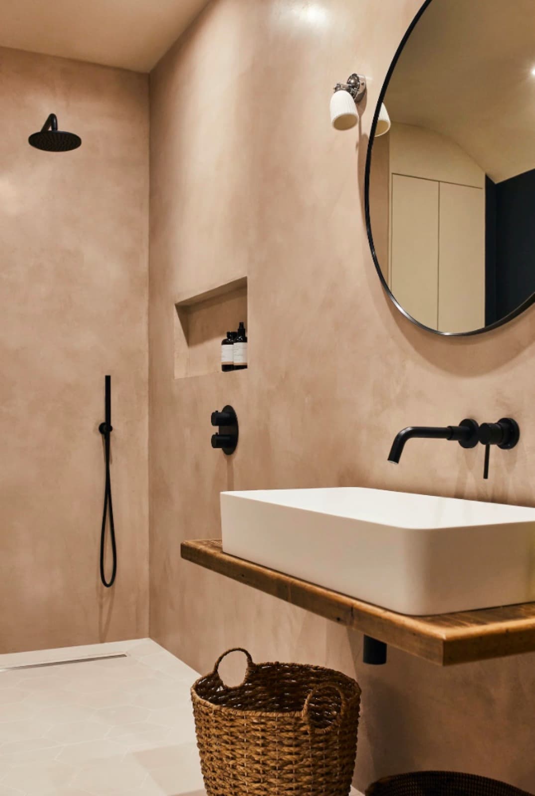 Tadelakt bathroom in warm clay pink, seamless from shower wall to vanity, with a wall-hung basin and black fittings